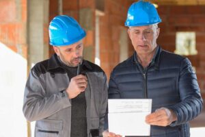 Workers install cabinets in a protected home interior while tools and construction materials sit nearby.