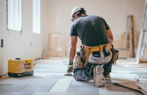 Homeowners review renovation plans beside a protected kitchen workspace with tools and building materials.
